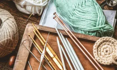 Spools of different coloredd yarn and twine sit on a wooden table. A wooden tray holds metal tools for knitting and crocheting.