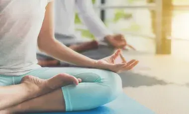 Two people seated on a floor in a yoga position with sunlight shining.