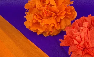 Close up of paper marigolds against a deep purple background.