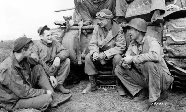 Ernie Pyle sits alongside soldiers