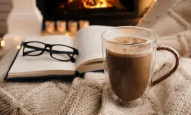 An open book with a cup of hot chocolate next to it 