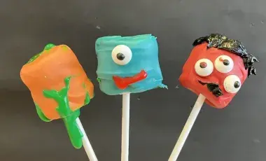 Three candy coated and decorated marshmallows: orange, blue, and red