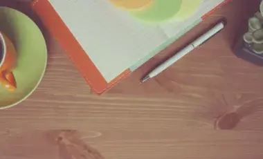 Mug of tea, open notebook, pen, and small plan on top of a wooden surface