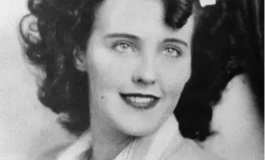 Black and white photo of Elizabeth Short, better known as the Black Dahlia, smiling and gazing past camera wearing a light colored suit jacket.
