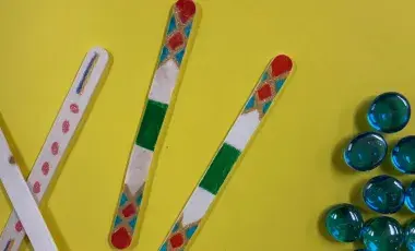 Four popsicle sticks with multicolored designs on them and a cluster of blue marbles