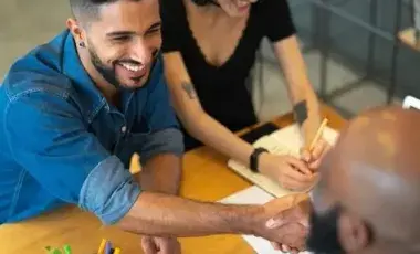 Man sitting across from two people shaking hands