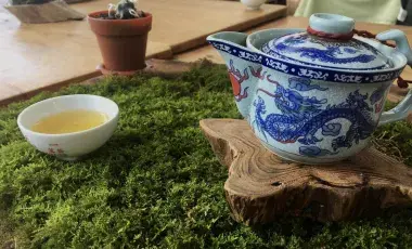 A cup of tea on the left and a blue and white tea pot sitting on a wood log on the right