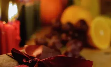 Red holiday candles and sliced fruits blurred out in the background with a gift with a red bow in the front.