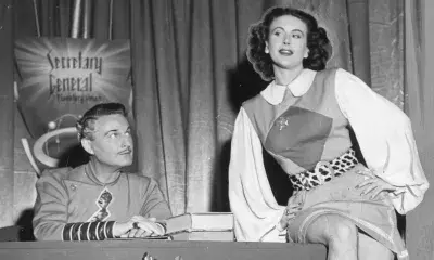 Nina Bara sits atop desk with person sitting behind