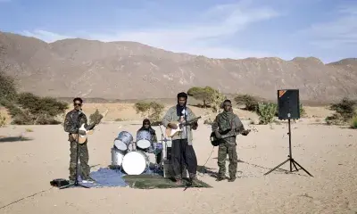 People wearing fatigues play in a band outdoors in a desert landscape