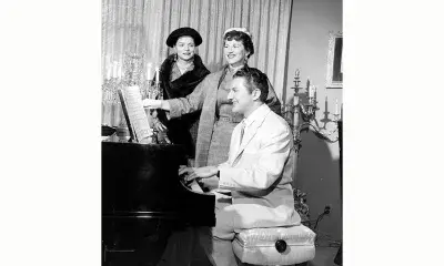 Person plays piano while two others sing along, 1956.