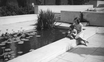 A mother and child sit on the ledge of the west reflecting pool of Central Library, ca 1937