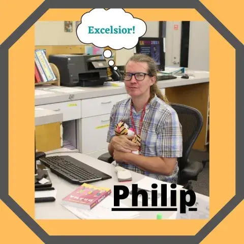 Philip sits at his desk at the library clutching a stuffed tiger.