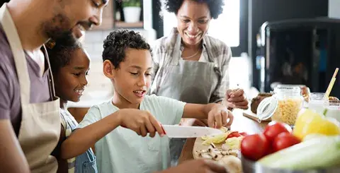 Young boy cutting vegetables with the family watching
