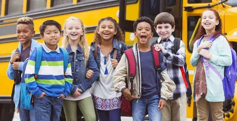 Happy, laughing diverse tweens standing near a school bus