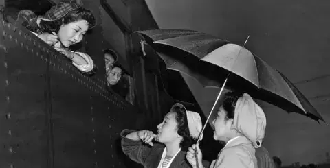 Young Japanese girls brave the early morning rain to bid farewell to friends leaving for Manzanar relocation camp