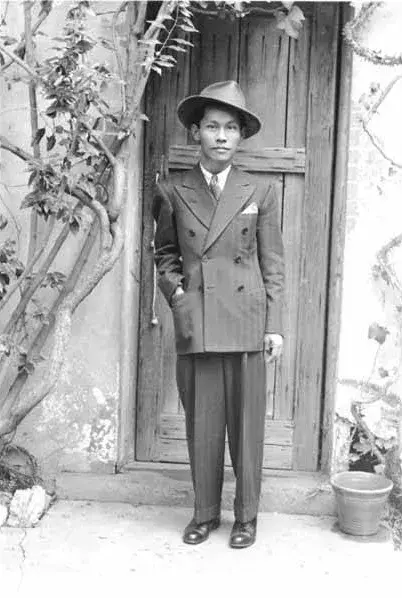 black & white photo of young man in a suit, standing in front of a door