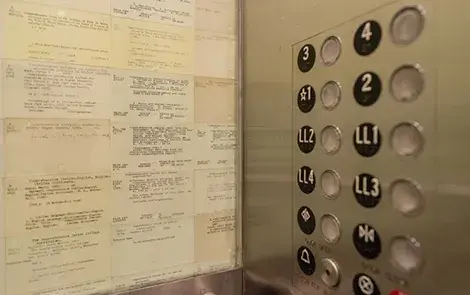 Interior of elevator wall with a display of card catalogs on the left and the buttons on the right.