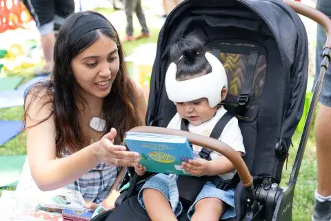 Parent helps baby in stroller hold book