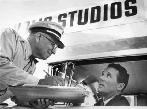 Republic Studios guard Leo Lotito greets actor Howard Duff as he arrives for work.