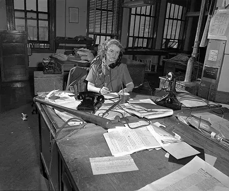 Aggie Underwood at her desk with a baseball bat next to a telephone