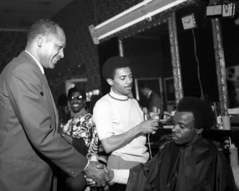 	 Councilmember Tom Bradley (at left) is shown shaking hands with an unidentified man sitting in a barber
