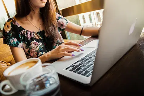 a young woman looking at her apple laptop with a coffee cup next to her on her desk