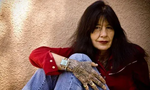 Joy Harjo wearing a red shirt and jeans showing her tattooed hand