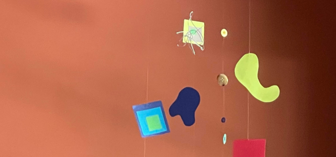 colorful shapes and buttons hang in a mobile in front of a brown background