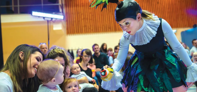 Woman with bird puppet interacting with audience of adults & children