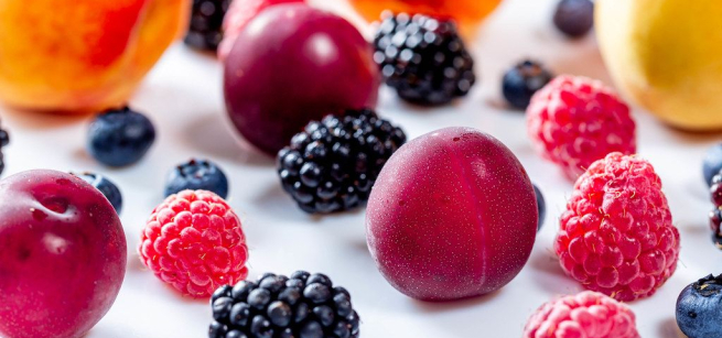 variety of stone fruit and berries scattered on white surface