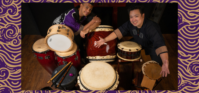 Two musicians next to several drums