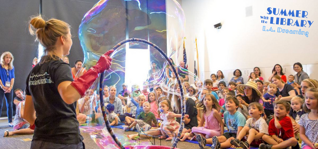 Seated audience watching a woman perform a big bubble trick
