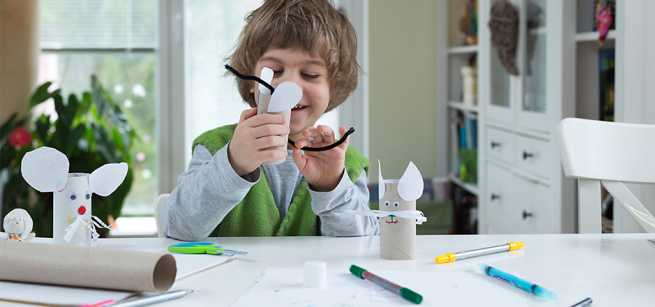 A child is gluing a pipe cleaner to a cardboard core for a craft.