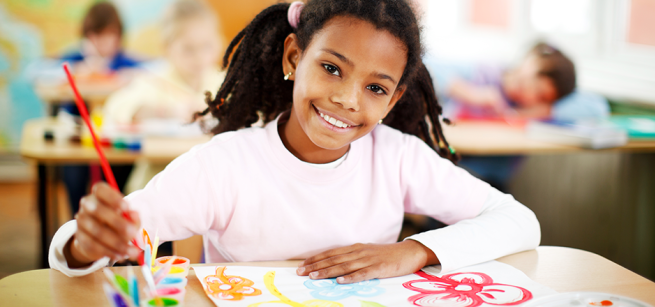 A young girl sits at a table while painting flowers on paper.