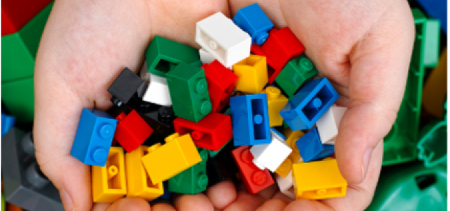 Two hands cupped together hold many small building blocks over a background of blurred building blocks.
