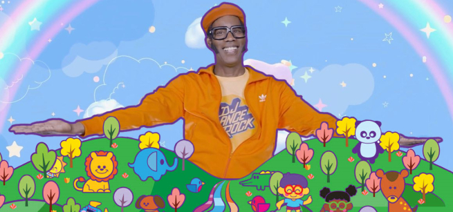 DJ Lance Rock stands in behind a grassy hill covered in colorful animals and trees