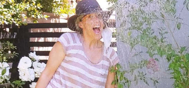 Sarah Klein smiling and spraying water with a garden hose