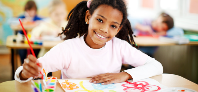 Child looking up and smiling into camera while she paints a picture