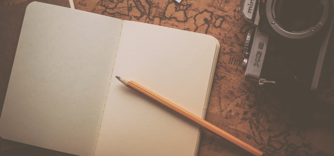 travel journal, camera, and pencil on top of a vintage map
