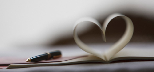 A black pen rests on an open book with pages folded to resemble a heart shape