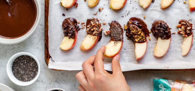 picture of a hand placing an apple slice on a tray of apples dipped in chocolate
