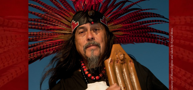 Martin Espino dressed in an indigenous costume, holding an instrument.
