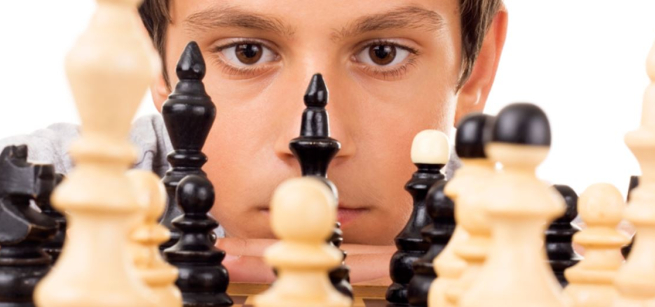 Young boy looking at chess pieces.