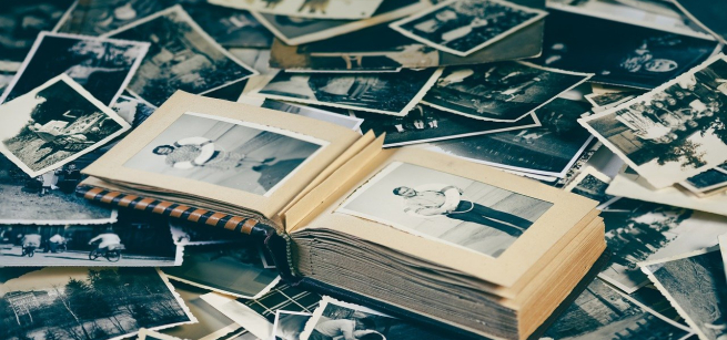 An antique family photo album sits atop a pile of black and white photographs.