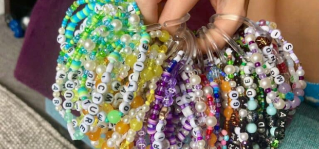 A person's hand is shown holding a wide variety of alphabet friendship bracelets.