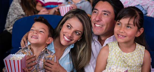 Mother, father, son and daughter looking at movie screen with popcorn