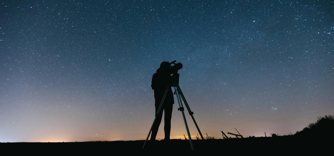 a person with a telescope backlight with the night sky