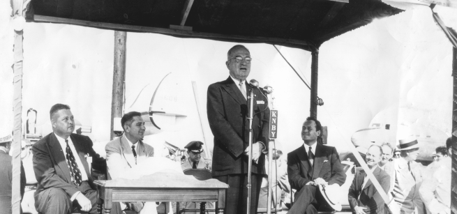 man speaking into the microphone surrounded by people