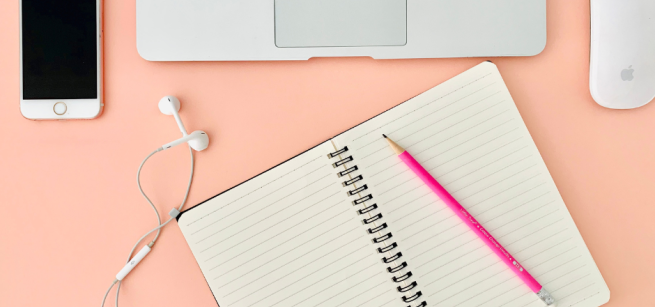 open notebook with pen on top in front of a laptop and phone